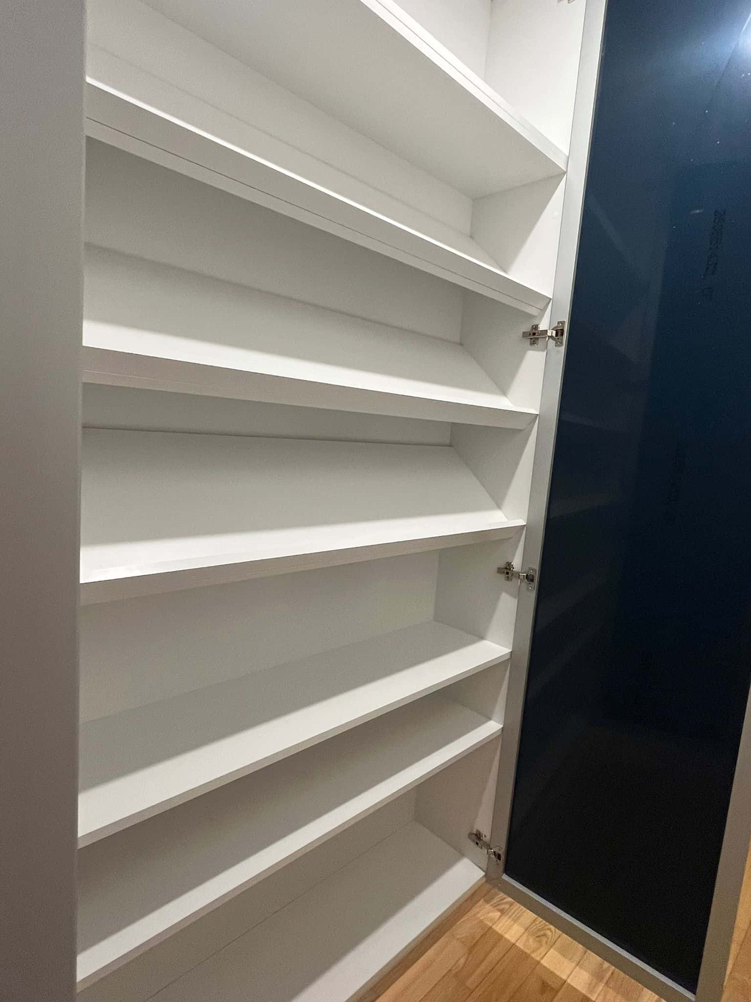 Półka na buty w szafie z białymi półkami i czarnymi drzwiami